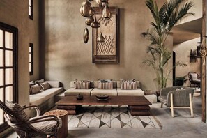 A cozy living room with a sofa, coffee table, and chairs, featuring a large plant and decorative wall art.