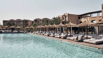A poolside area with lounge chairs and umbrellas, surrounded by buildings with palm trees.