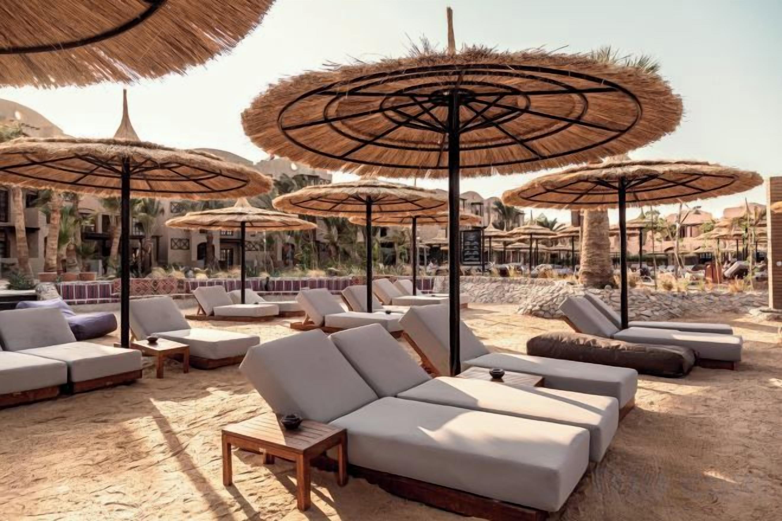 A beachside lounge area with sun loungers and thatched umbrellas.