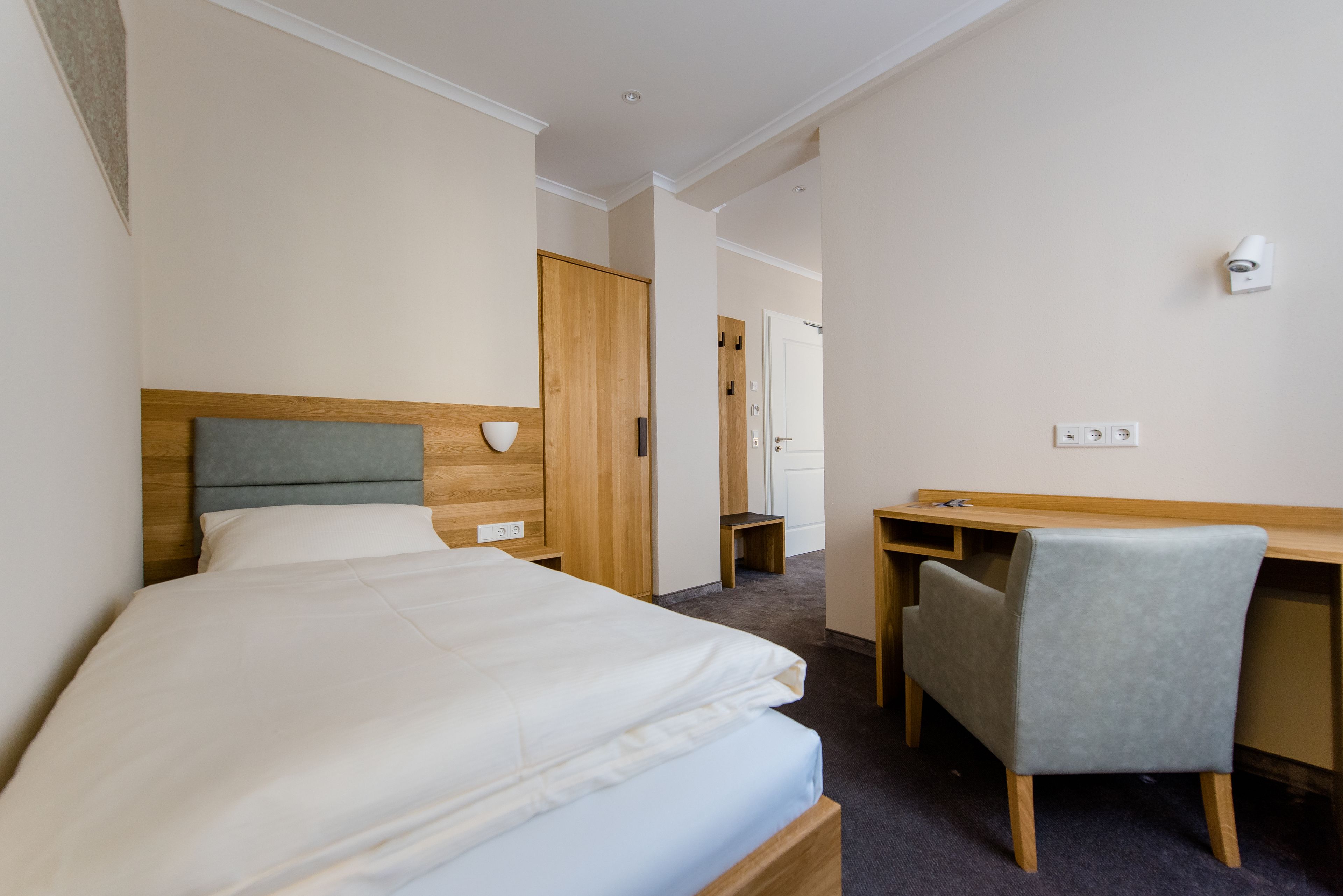 A hotel room with a bed, a desk, a chair, and a wardrobe.