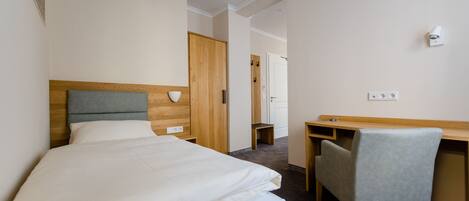 A hotel room with a bed, a desk, a chair, and a wardrobe.