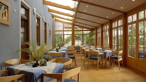 A spacious dining area with wooden tables and chairs, large windows, and a high ceiling. - Gasthaus Sindel-Buckel Herrenhaus (Feuchtwangen)