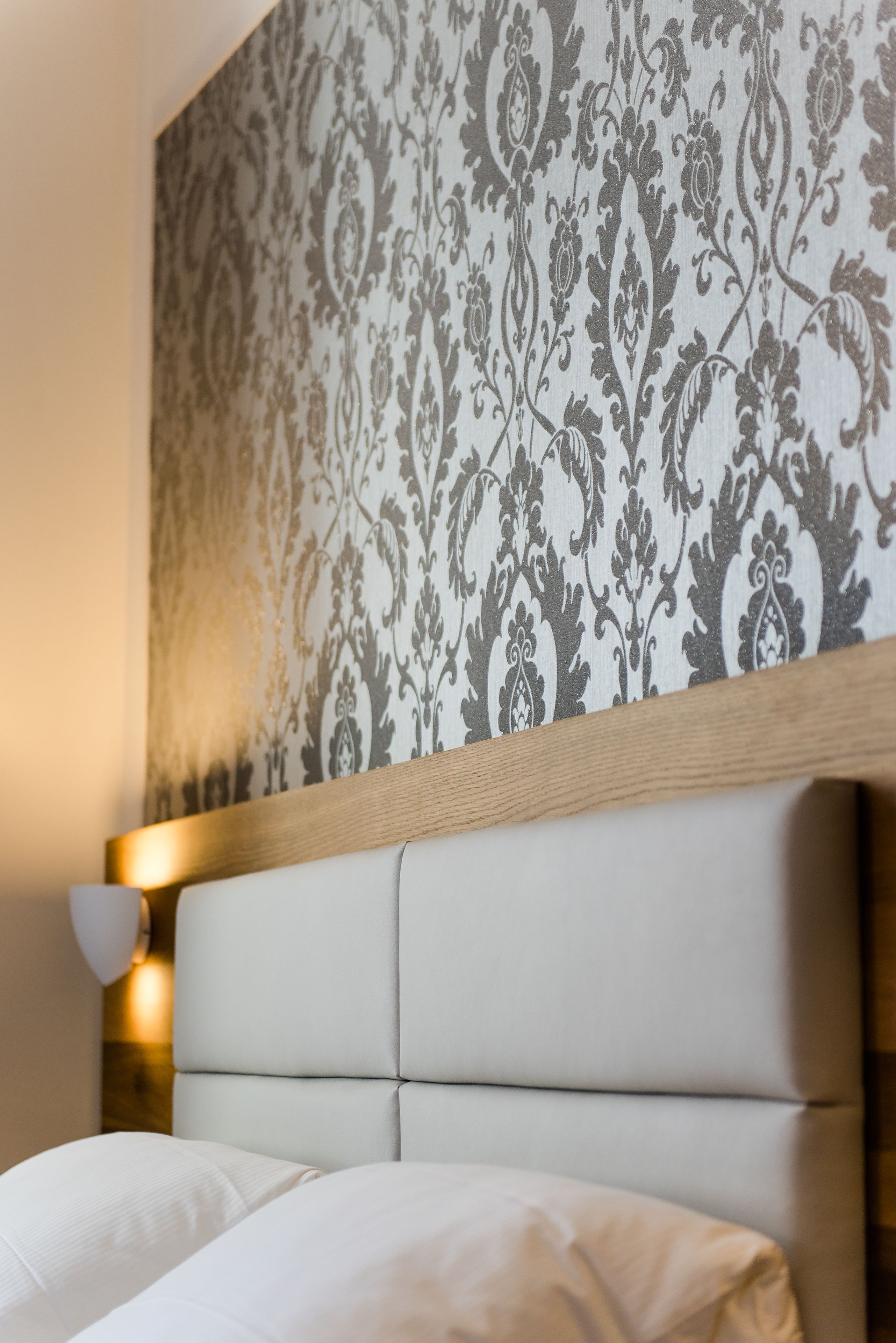 Un dormitorio con papel tapiz estampado, cabecero de madera y lámpara de noche.
