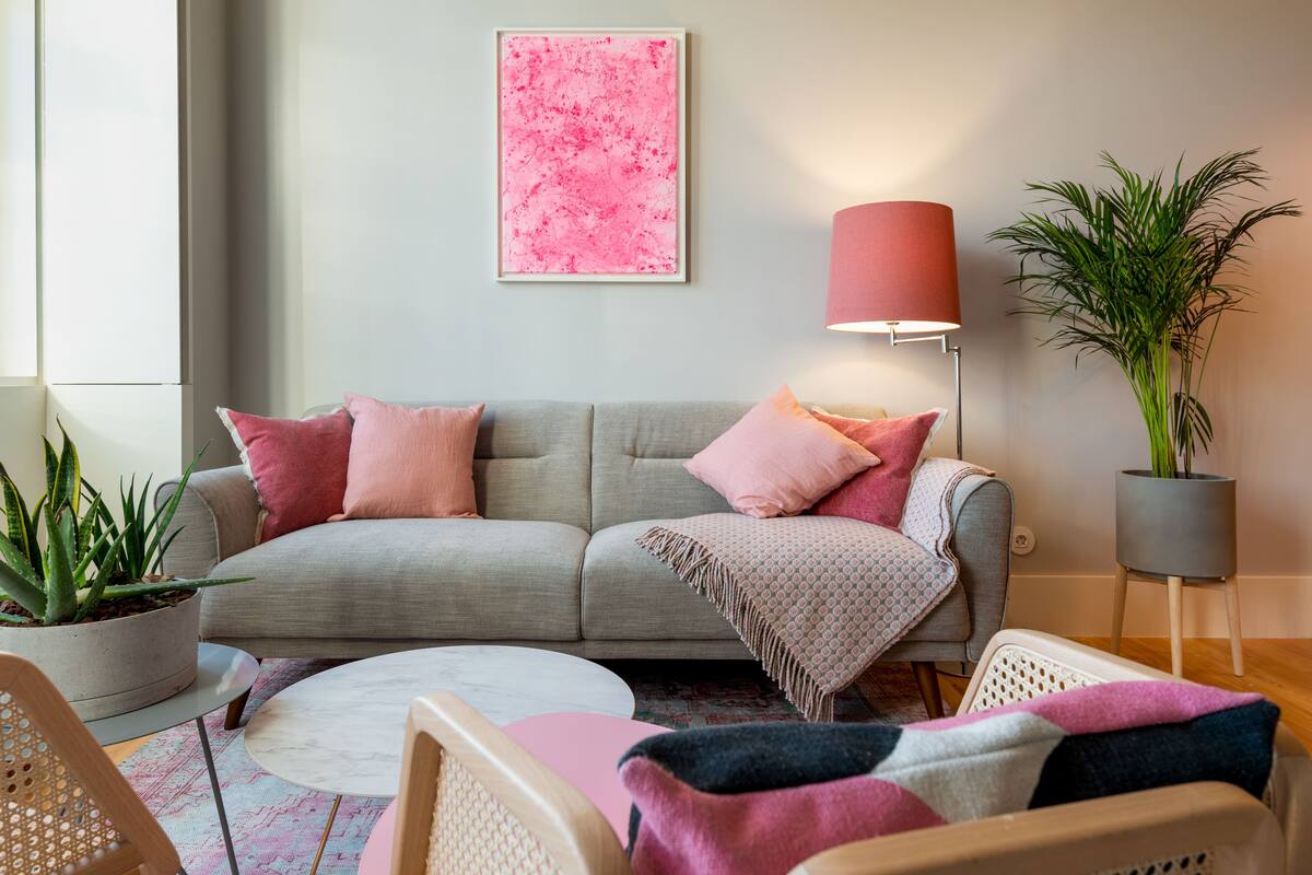 Una sala de estar con un sofá gris, cojines rosados, una mesa de centro redonda y una lámpara de pie.