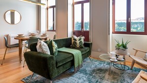 En moderne stue med en grøn sofa, et spisebord med stole og store vinduer med udsigt.