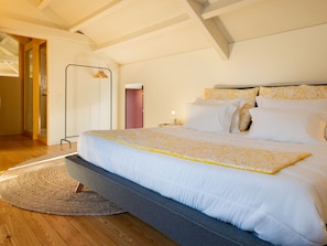 Un grand lit recouvert d’une couvre-lit à motifs blancs et jaunes, un banc rembourré de couleur grise et un plancher en bois.