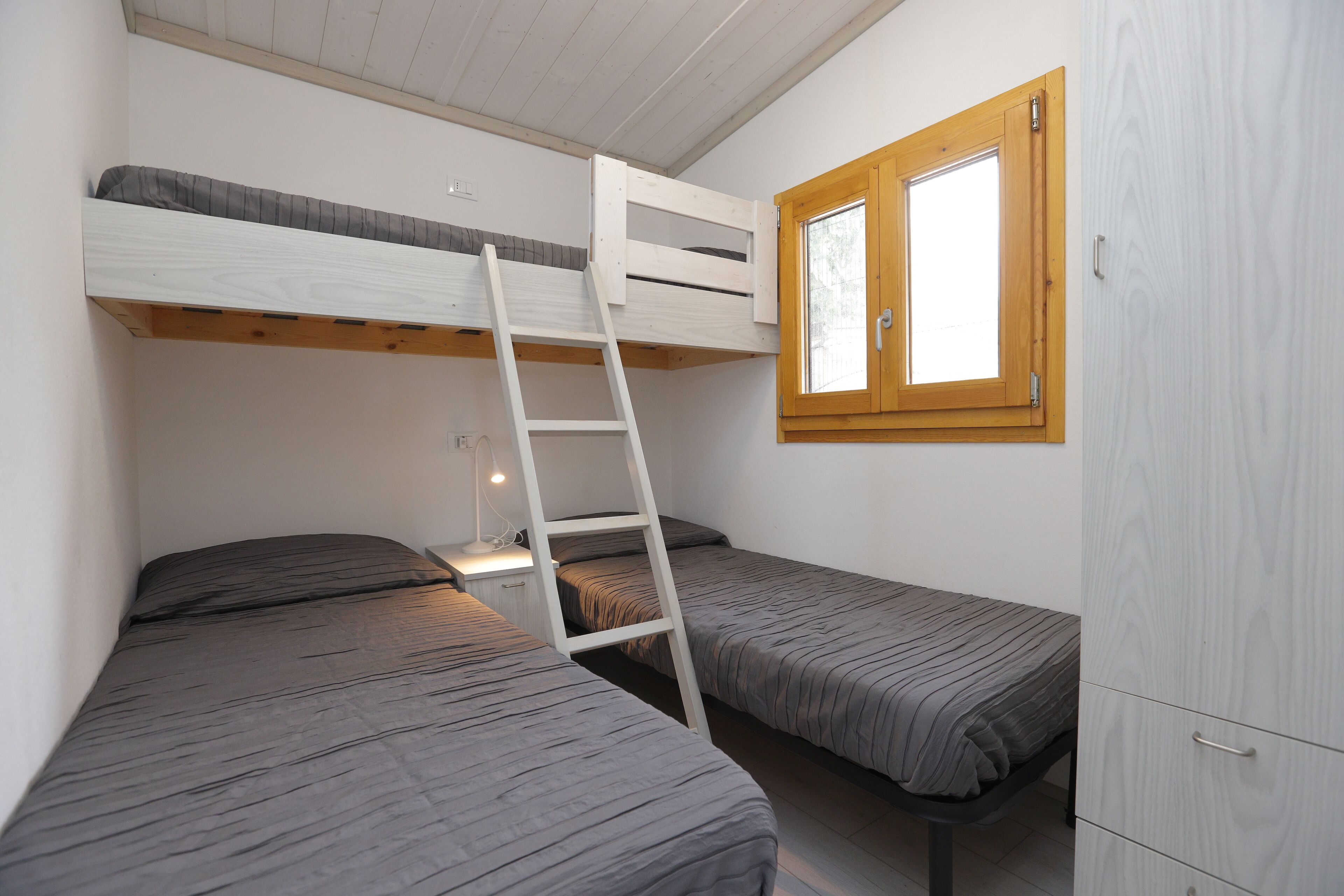 A dormitory room with bunk beds, a ladder, a window, and a wardrobe.