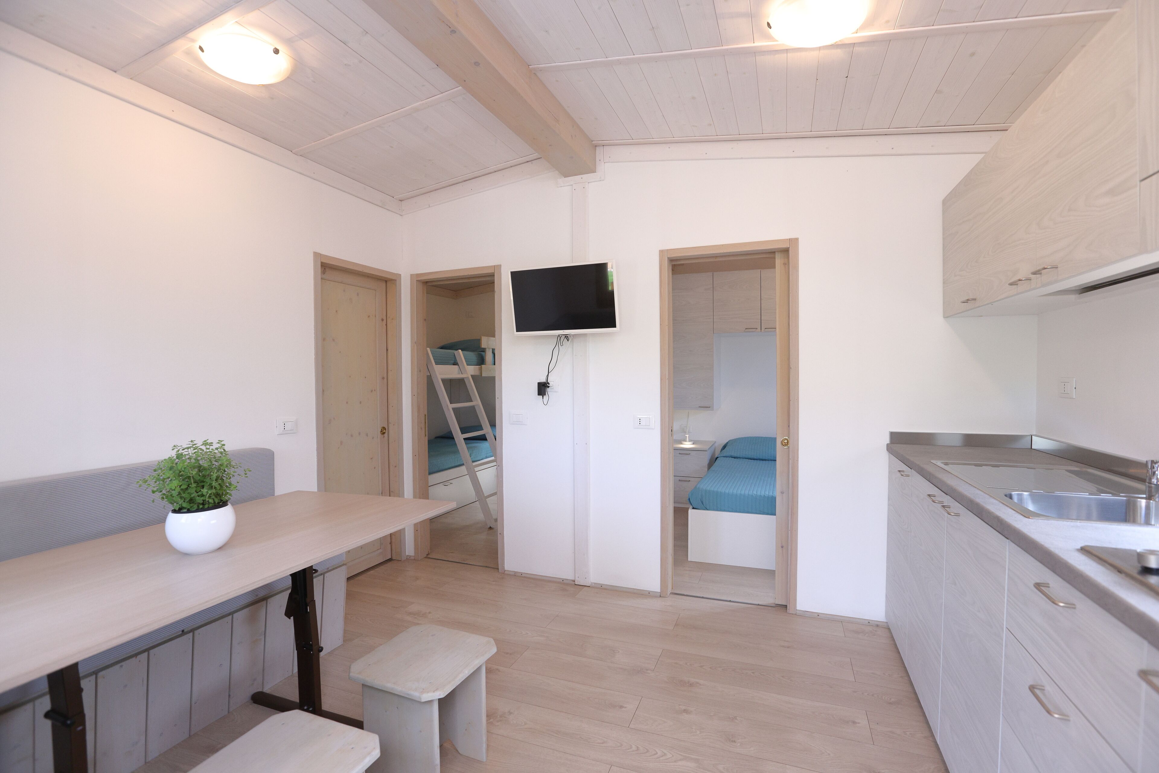 A compact kitchen with a built-in TV, wooden cabinets, and a bench.