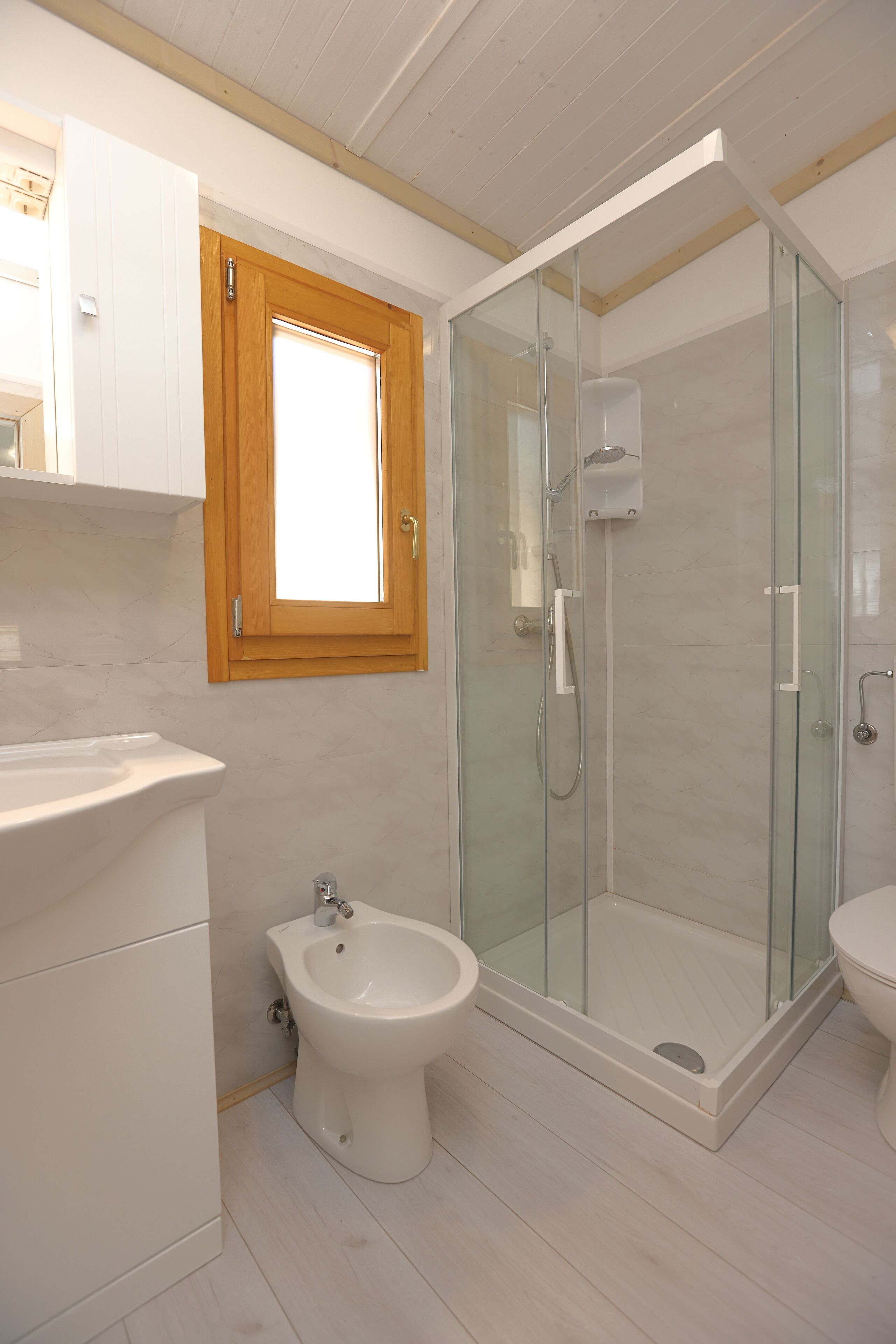 A modern bathroom with a glass-enclosed shower, a bidet, and a toilet.