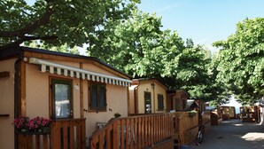 A row of wooden cabins with balconies, a covered walkway, and a bicycle parked nearby. - Parco Vacanze Lo Scoglio (Lavagna)