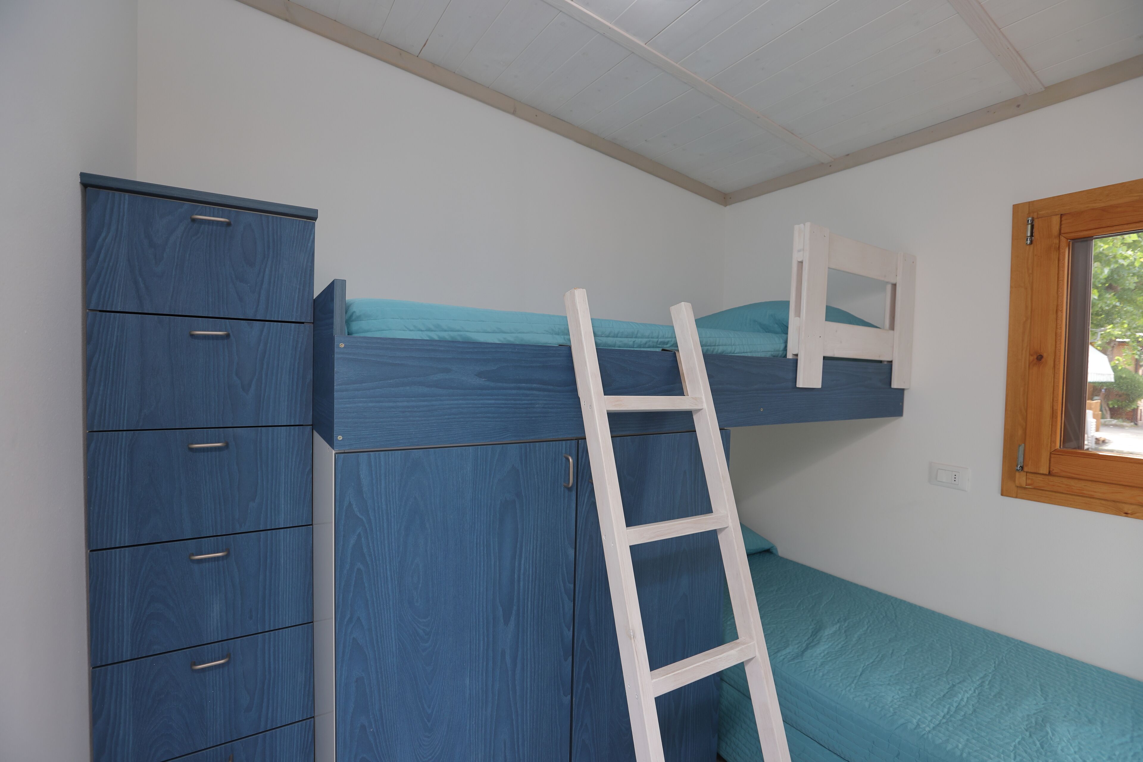 A room with a bunk bed, a wardrobe, and a window.