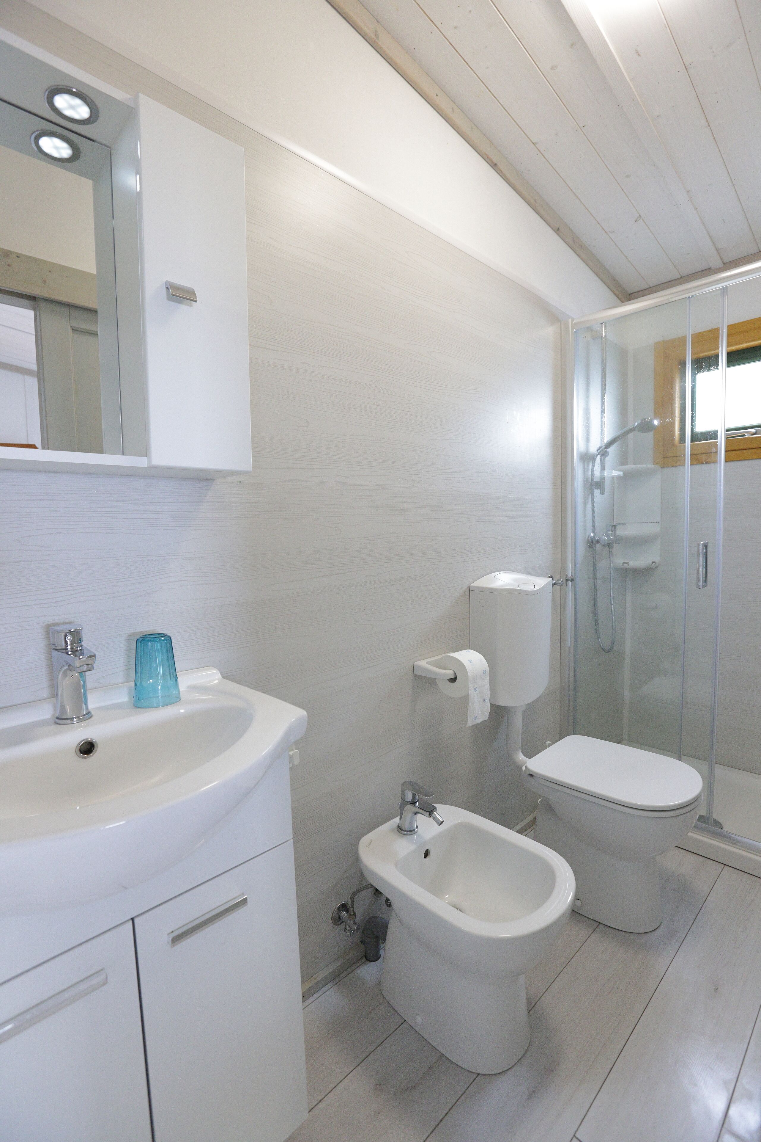 A modern bathroom with a white sink, bidet, toilet, and glass-enclosed shower.