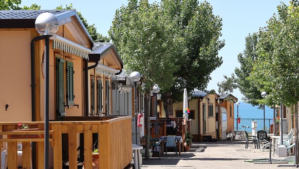 A row of wooden cabins with balconies, a table, chairs, and a small garden area. - Parco Vacanze Lo Scoglio (Lavagna)