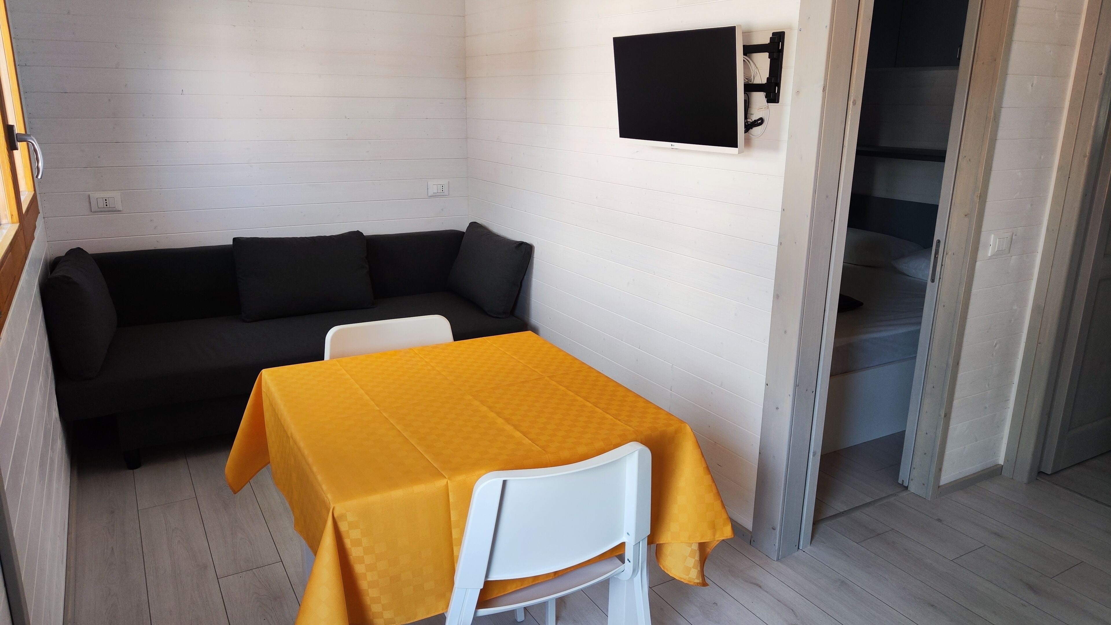 Ein Zimmer mit einem weißen Sofa, einem gelben Tisch und einem an der Wand befestigten Fernseher.