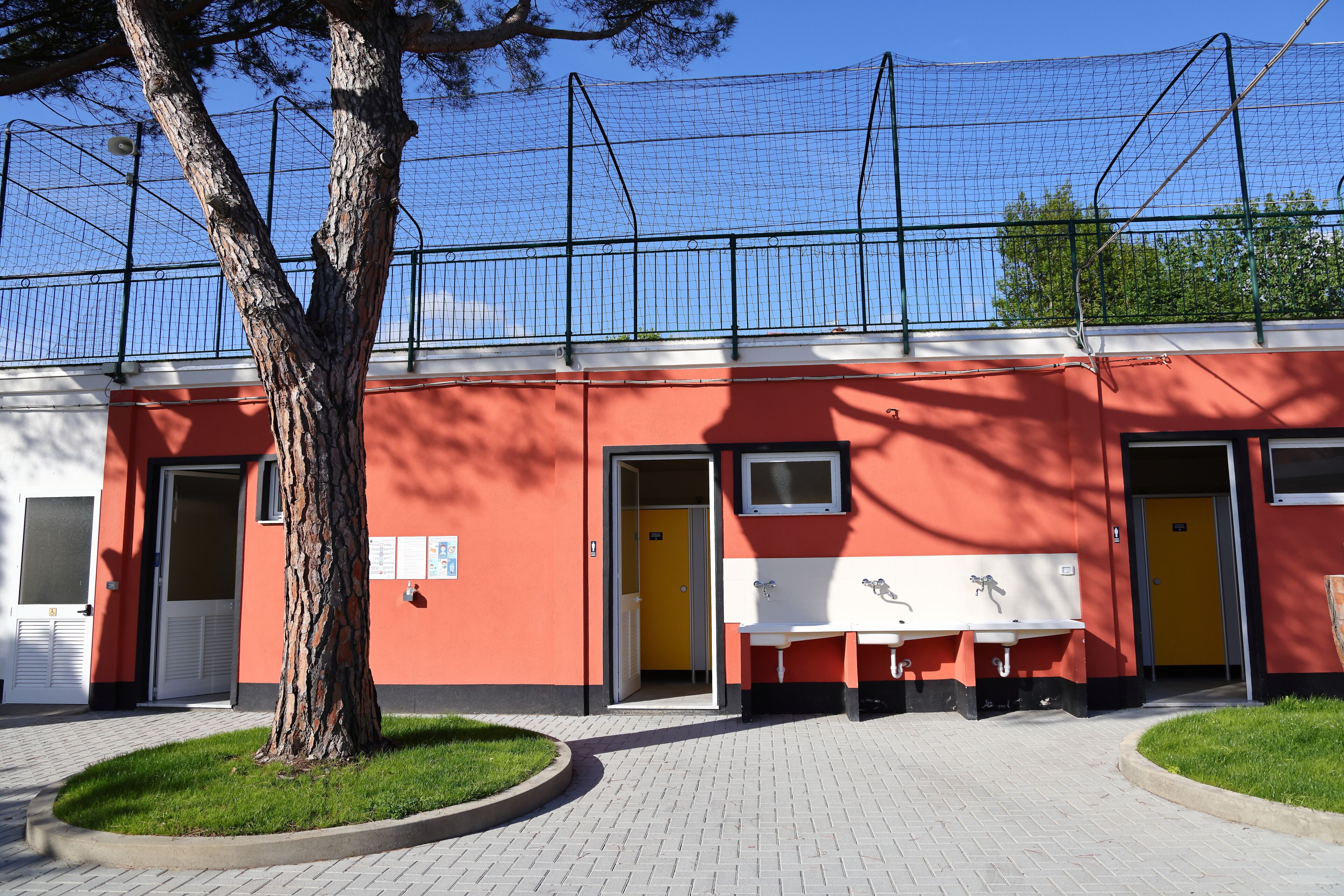 Ein Gebäude mit roter Fassade, ein Baum davor und eine Bank mit einem Schild.