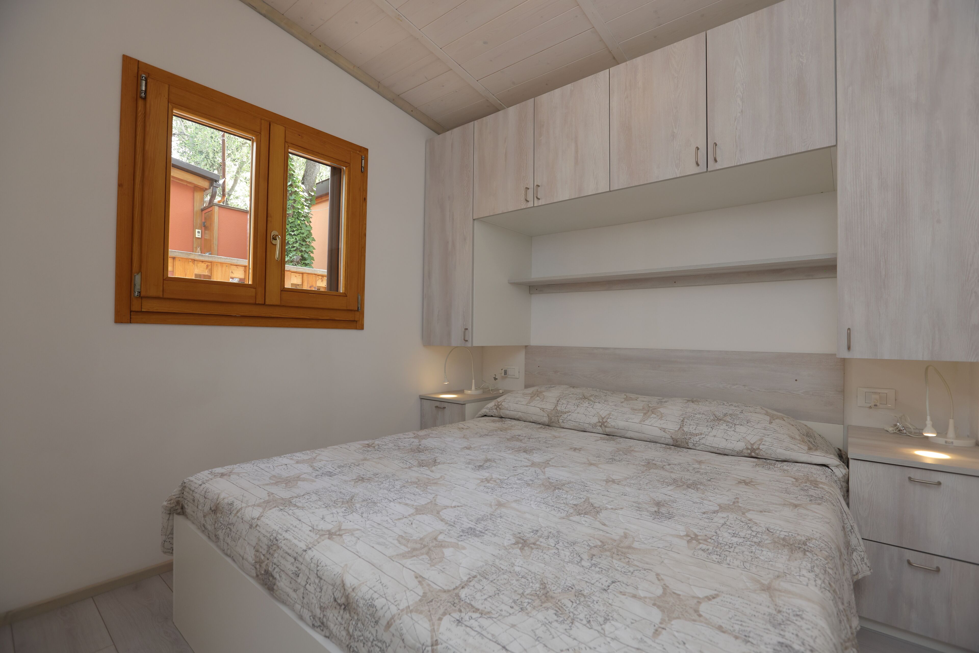 A bedroom with a bed, a window, built-in shelving, bedside tables, and a nightstand.
