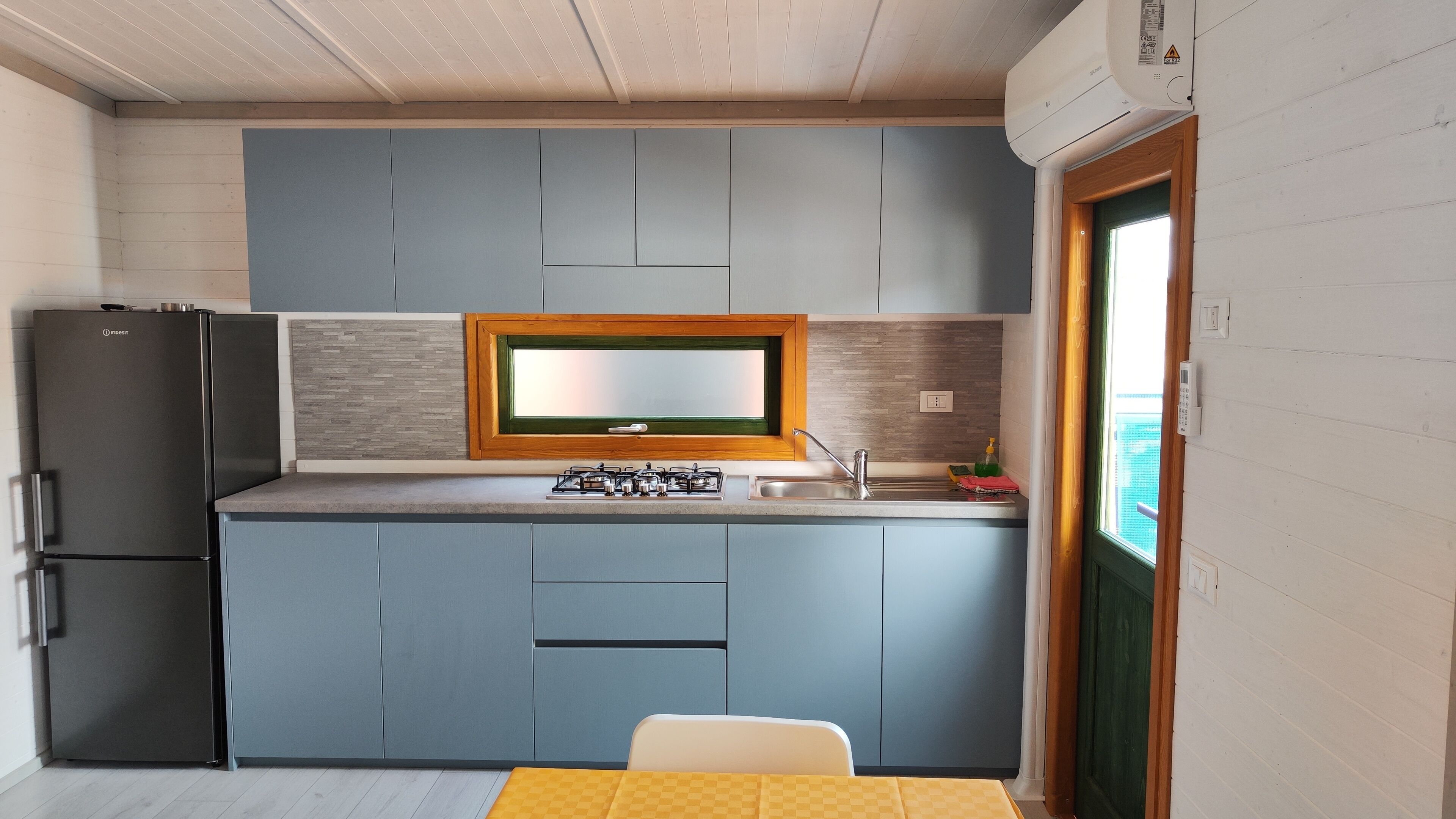 A compact kitchen with a built-in gas stove, a refrigerator, and a window with a view.