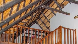 Una escalera de madera con barandilla, un armario de madera y un sofá amarillo en una habitación con suelo de baldosas.