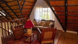 Acogedor dormitorio en ático con techo inclinado, escalera de madera, lámpara roja, sofá y alfombra estampada.