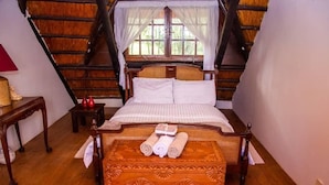 Una cama con toallas enrolladas, un cabecero de madera y una ventana con cortinas.
