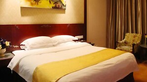Ein Hotelzimmer mit einem großen Bett, einem Kopfteil, einem Gemälde an der Wand, einem Sessel und einem Nachttisch mit Blumen.
