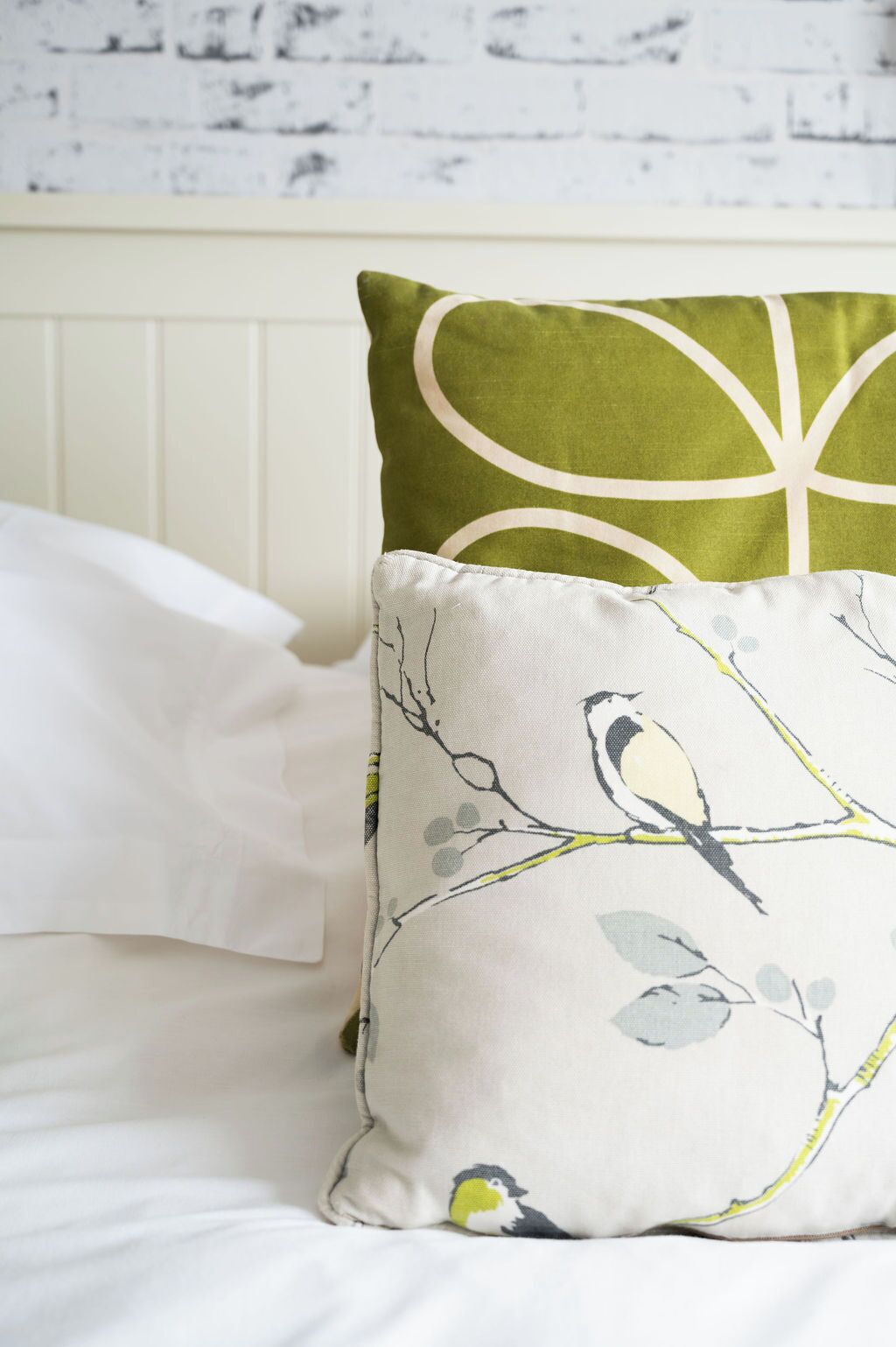 A bed with white bedding and two pillows, one with a bird pattern and the other with a circular design.