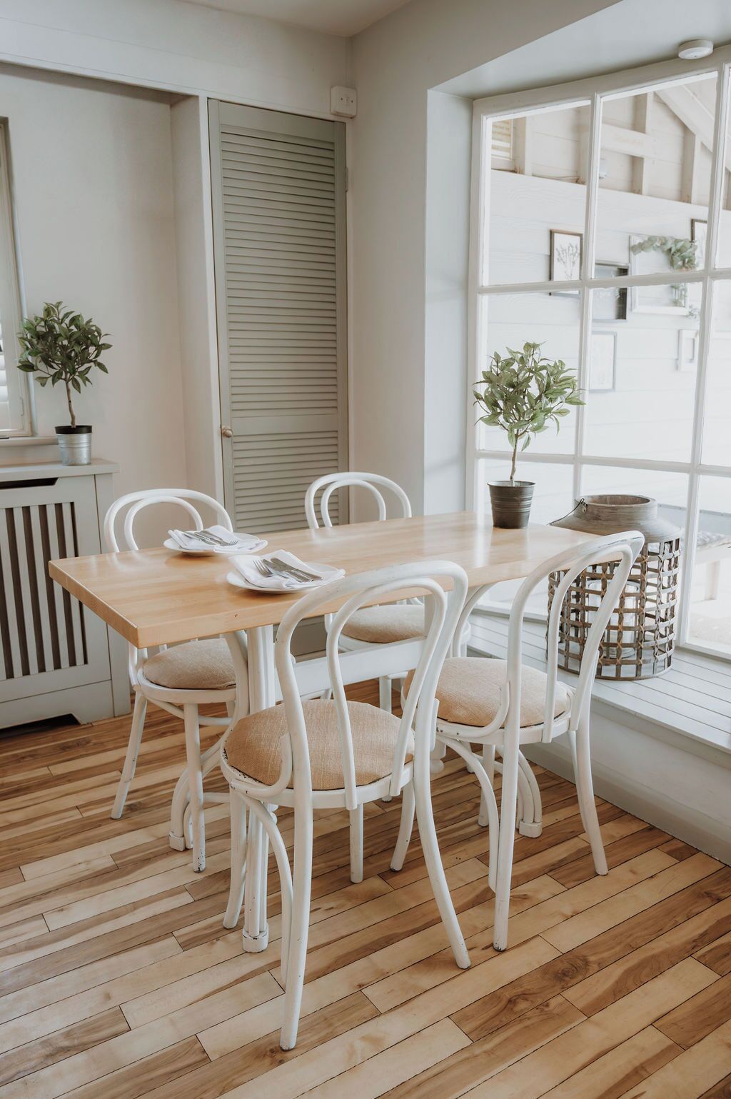 A room with a wooden floor, white furniture, a window with a view, and a radiator.