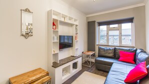 A modern living room with a flat-screen TV, a leather sofa with red cushions, a wooden coffee table, and a chandelier. - Luxury London Apartment 5-double rooms (London)