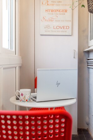 A laptop on a white table with a floral mug beside it, a red chair in the foreground, and a motivational quote on the wall.