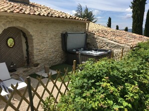 A stone building with a tiled roof, a hot tub, and a wooden fence. - La Lauren (Ferrassières)