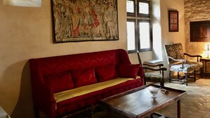 Een kamer met een rode bank, een houten tafel, een stoel en een groot historisch schilderij aan de muur.