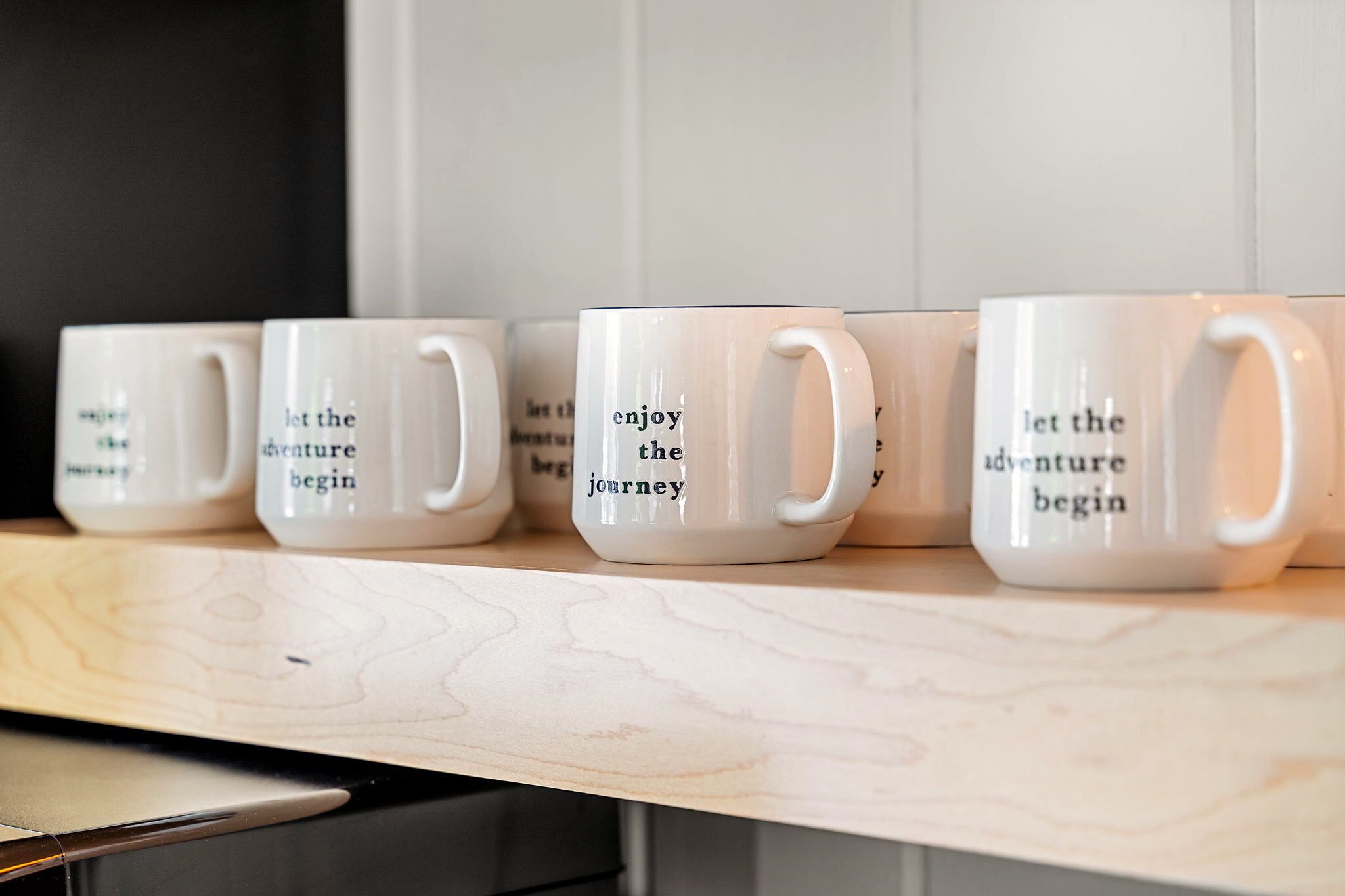 Una hilera de tazas de cerámica blanca con frases motivadoras sobre un estante de madera.