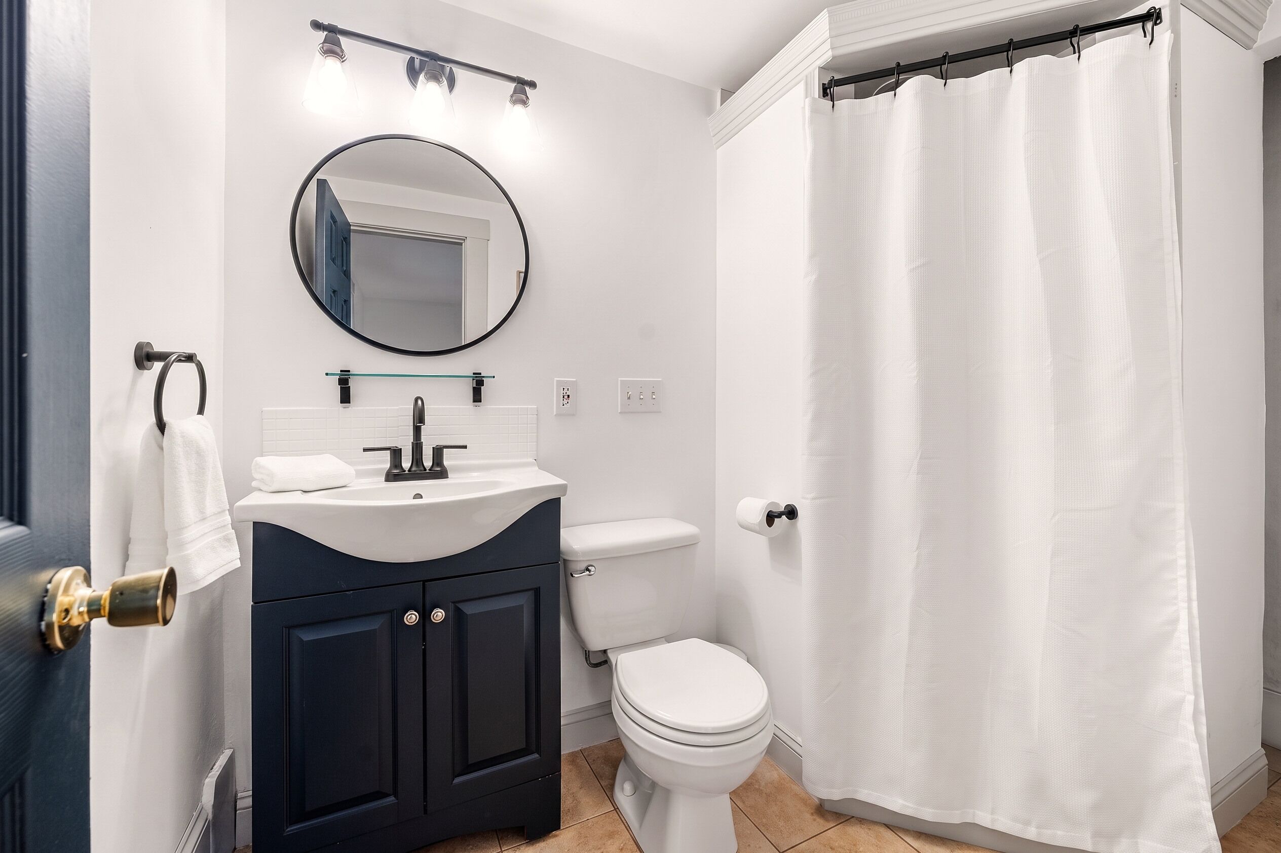 Un baño con inodoro blanco, tocador oscuro y cortina de ducha.