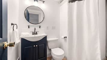Un baño con inodoro blanco, tocador oscuro y cortina de ducha.