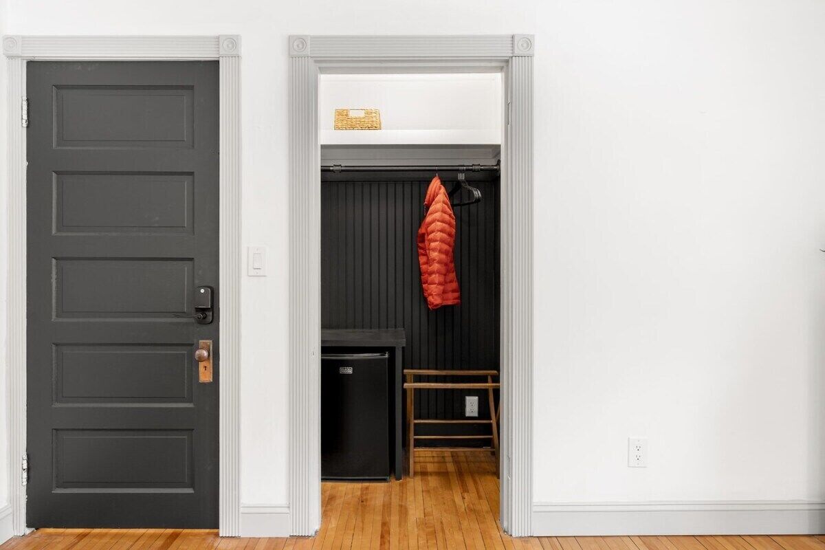 A room with a dark door, a small black refrigerator, and a red jacket hanging on a rack.