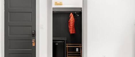 A room with a dark door, a small black refrigerator, and a red jacket hanging on a rack.