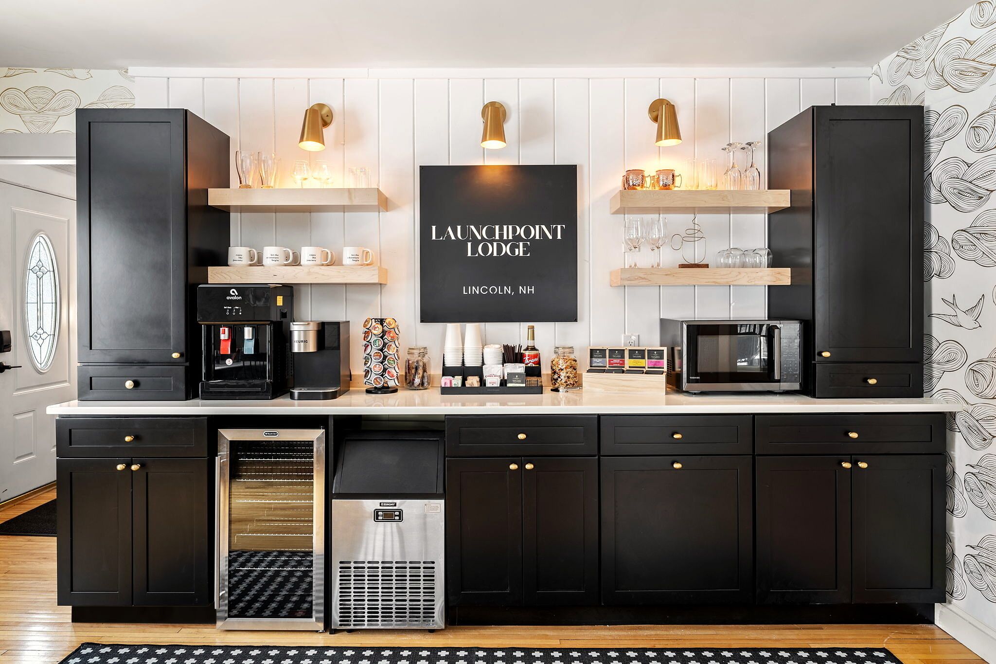 A modern kitchen with black cabinetry, a coffee machine, a microwave, and a sign reading 'LAUNCHPOINT LODGE LINCOLN, NH'.