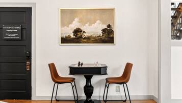 A room with a black door labeled 'LAUNCHPOINT LODGE Supply Closet,' a framed landscape painting, a chessboard, and two brown chairs.