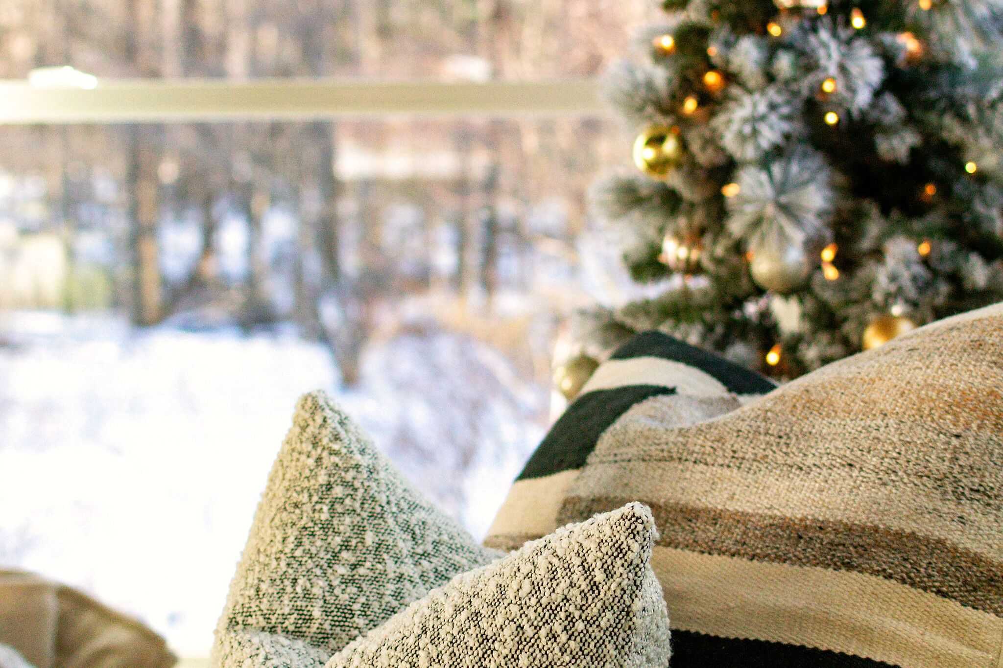 A cozy room with a view of a snowy landscape through a window, a decorated Christmas tree, and a striped throw blanket.