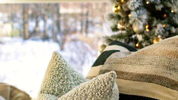 A cozy room with a view of a snowy landscape through a window, a decorated Christmas tree, and a striped throw blanket.