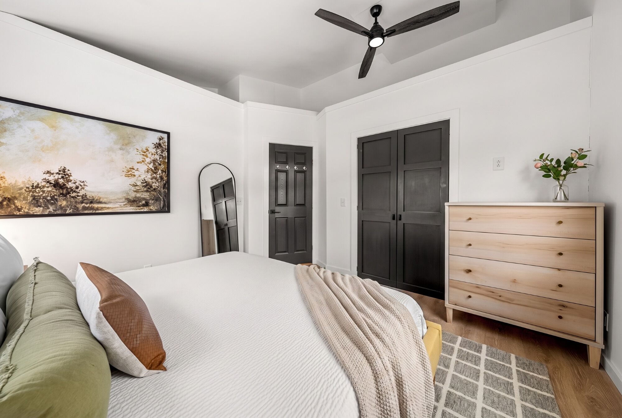 A bedroom with a bed, a dresser, a ceiling fan, and a door.