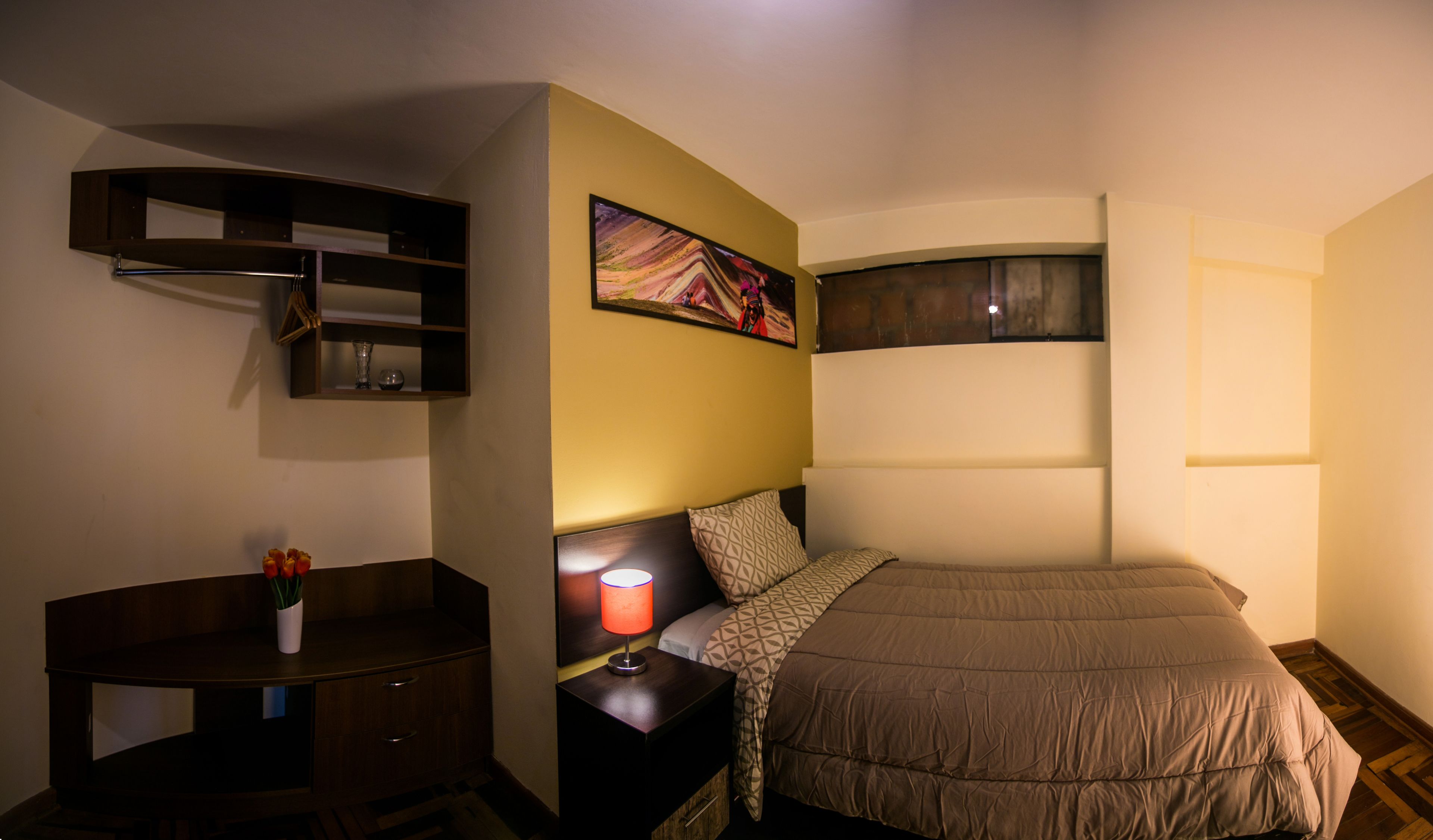 Un dormitorio con cama, mesita de noche, lámpara y estante con objetos decorativos.