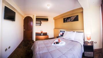 A hotel room with a bed, a nightstand, a TV mounted on the wall, a wooden door, and a painting on the wall.