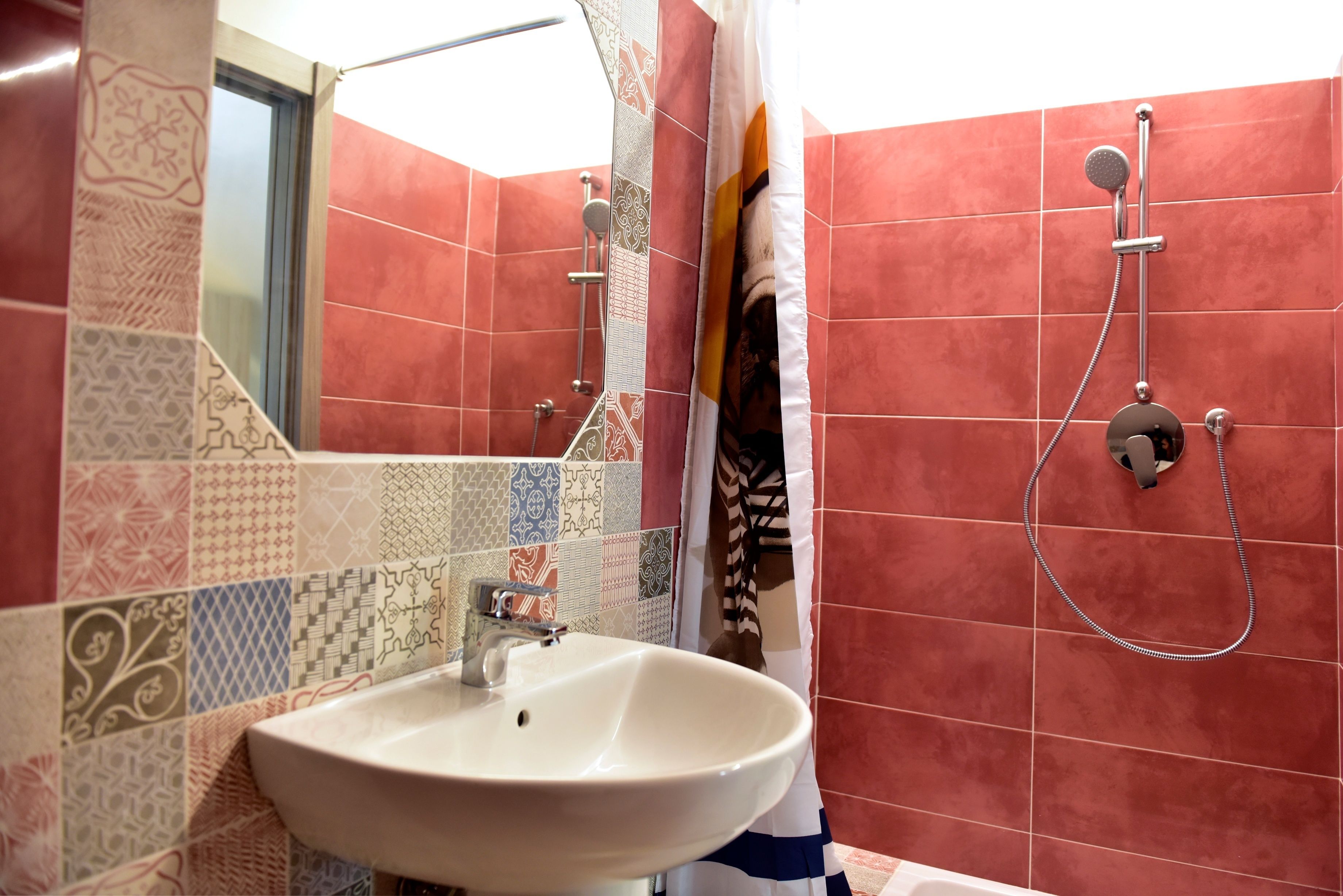 Une salle de bain avec un lavabo blanc, une douche équipée d’un pommeau de douche à main et un miroir au-dessus du lavabo.