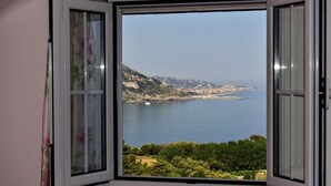 Habitación con un gran ventanal que ofrece vistas de un paisaje costero, incluyendo una playa y colinas.