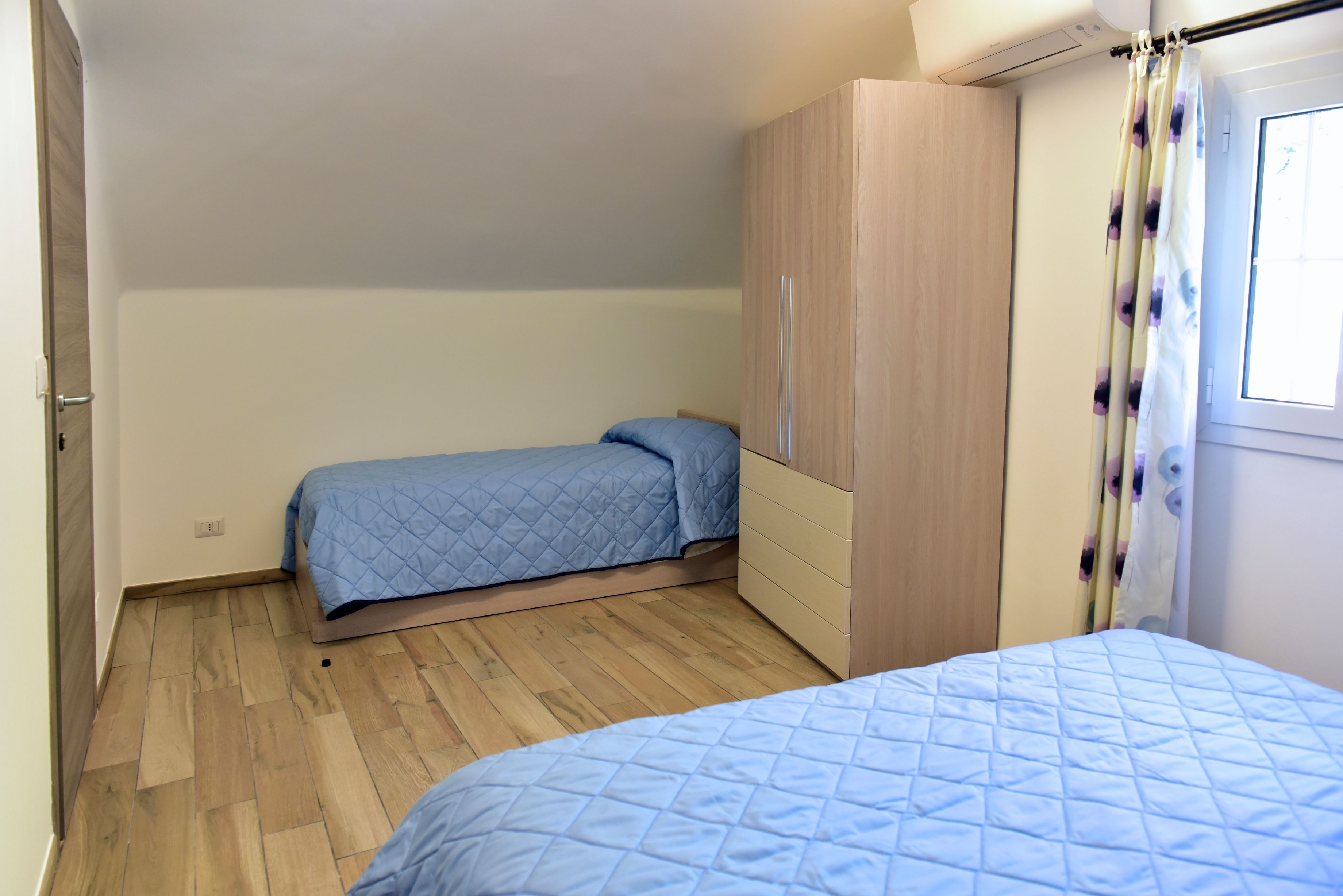 A bedroom with two beds, a wardrobe, and a window with curtains.