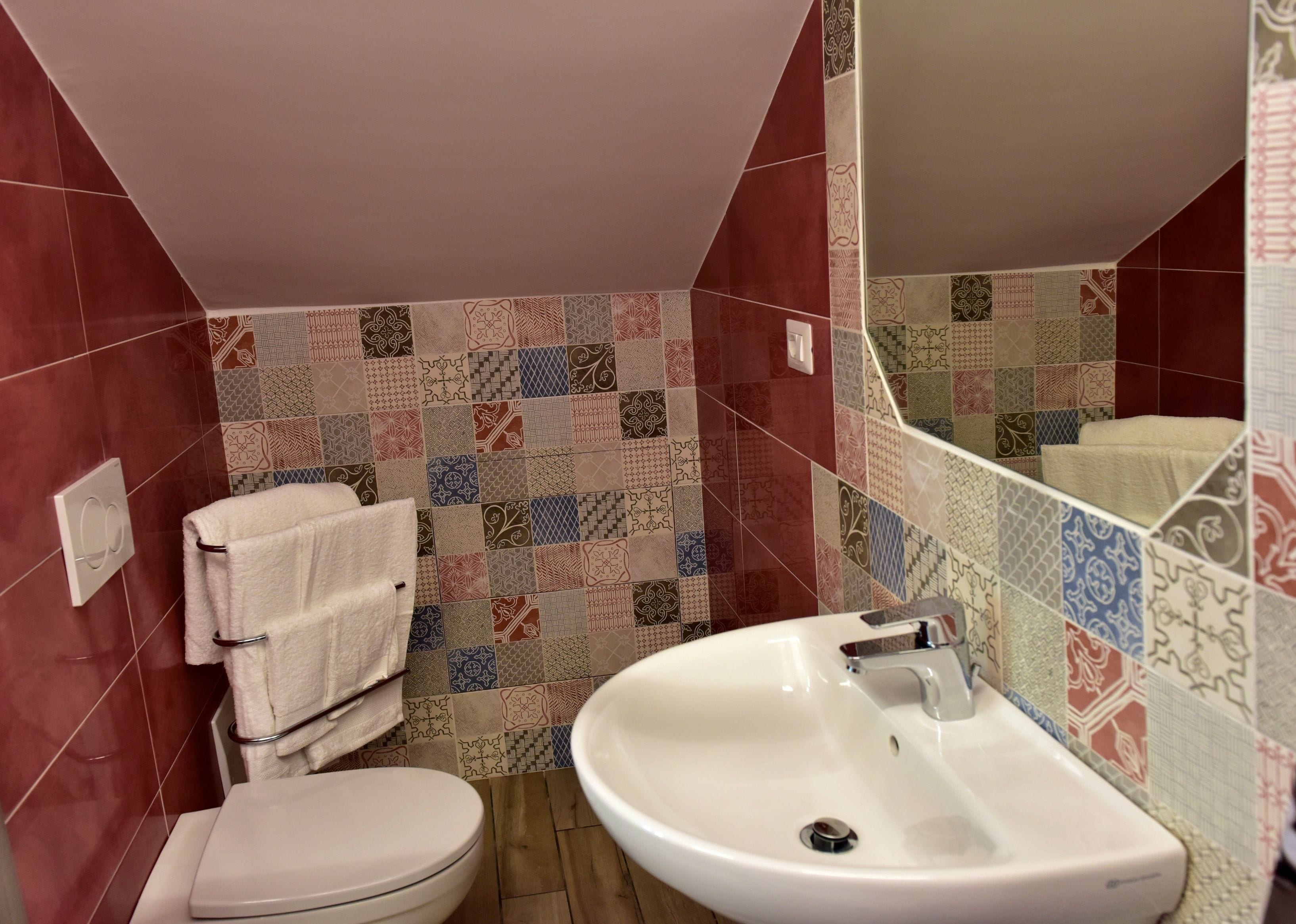 Un baño con inodoro, lavamanos y un revestimiento de baldosas con varios diseños.