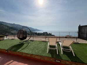 A terrace with artificial grass, two white lounge chairs, and a large speaker. A scenic view of the sea and hills is visible in the background. - Agriturismo Un Mare di Fiori (Ventimiglia)