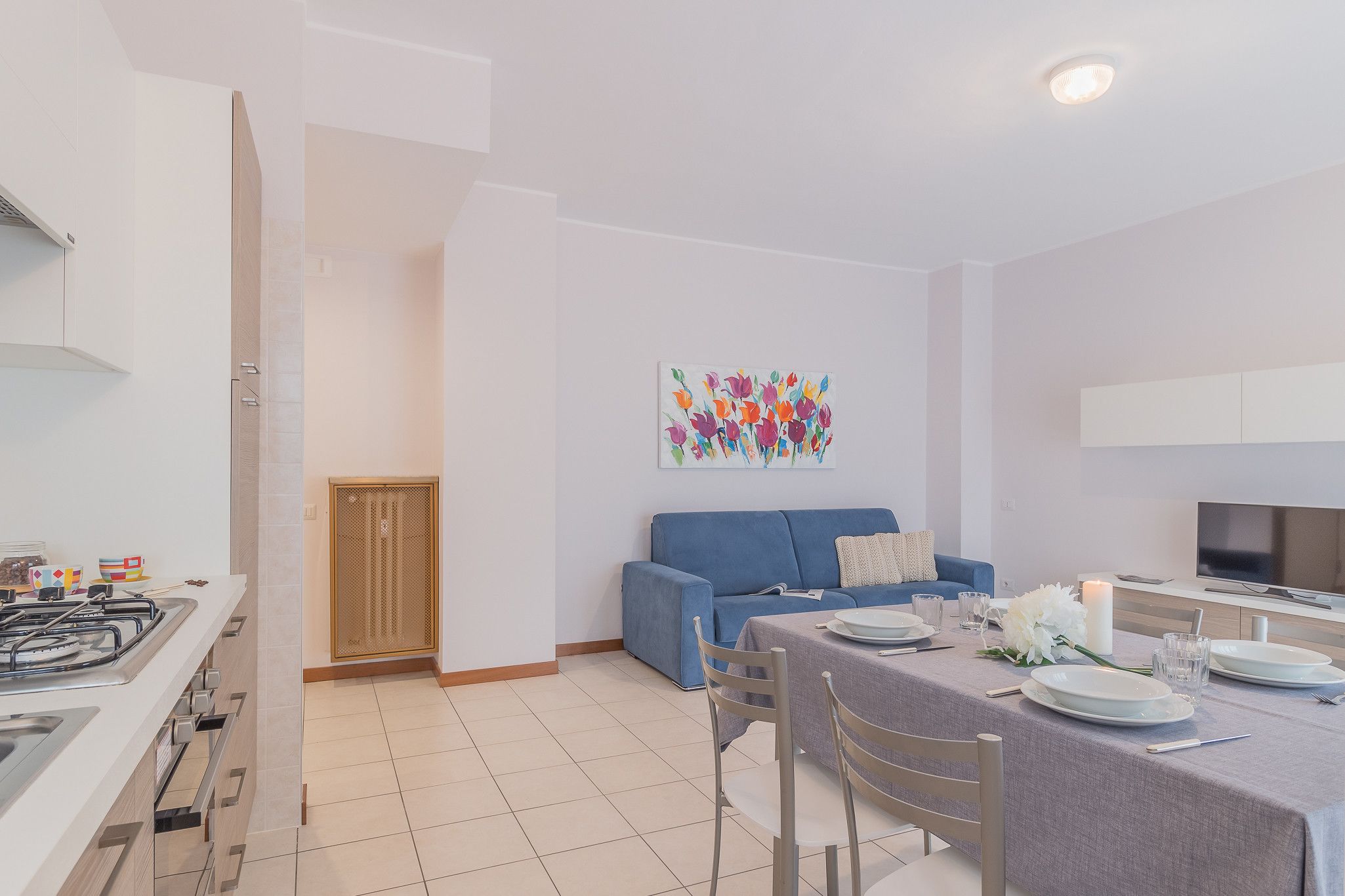 A modern kitchen with a gas stove, a dining area with a table set for two, and a blue sofa in the living area.