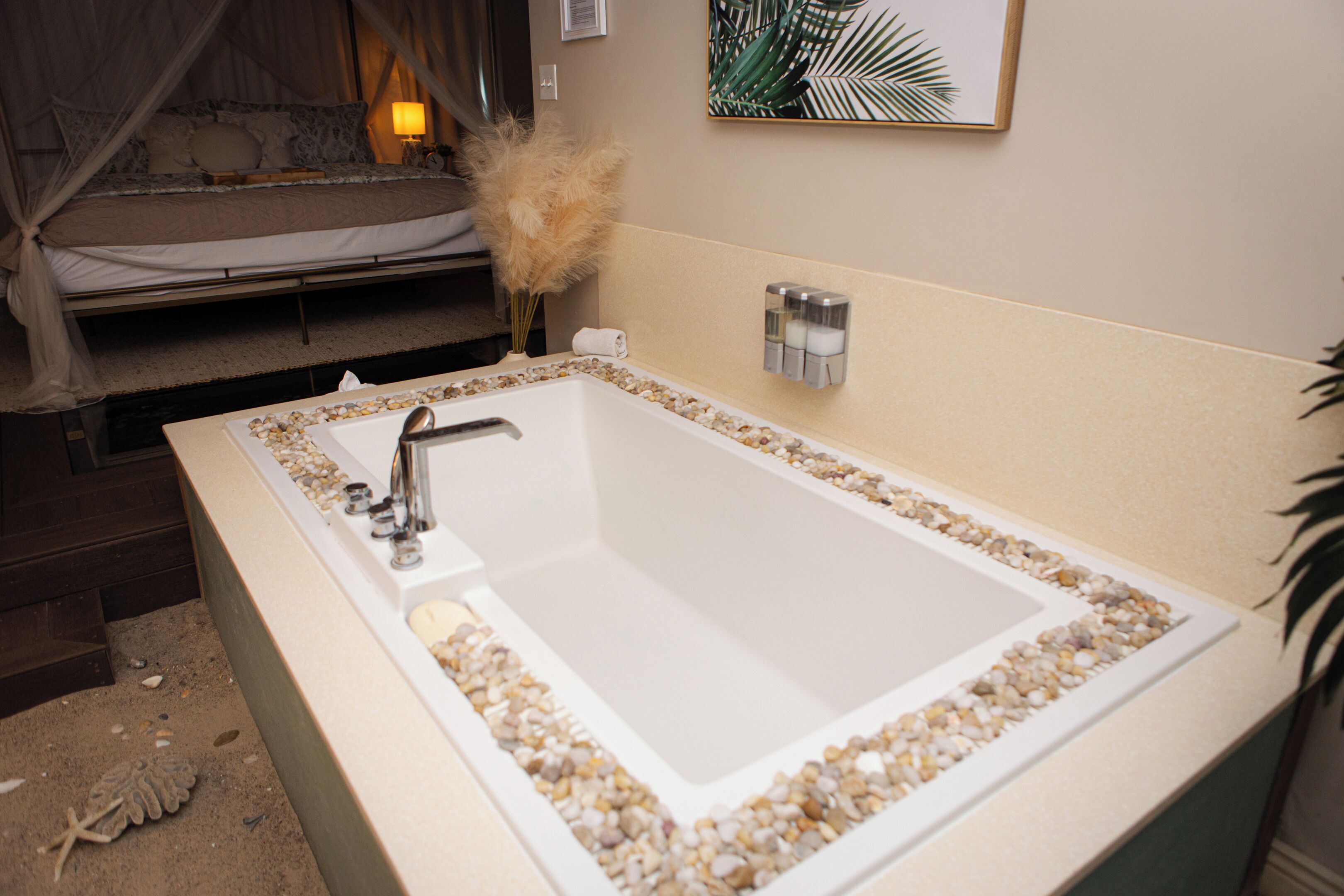 A bathroom with a bathtub surrounded by pebbles, a shower area, and a bed with a canopy.